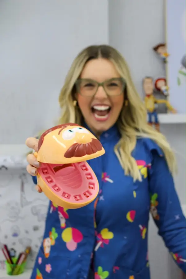 Dra. Juliana Lozano sorrindo e mostrando um macromodelo de dentes no consultório de odontopediatria na Lapa